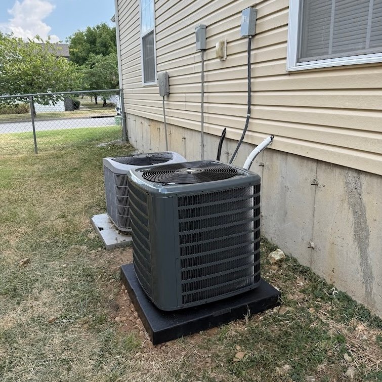 An Air Dynamics of Tulsa technician services an outdoor compressor unit beside a house in Tulsa.